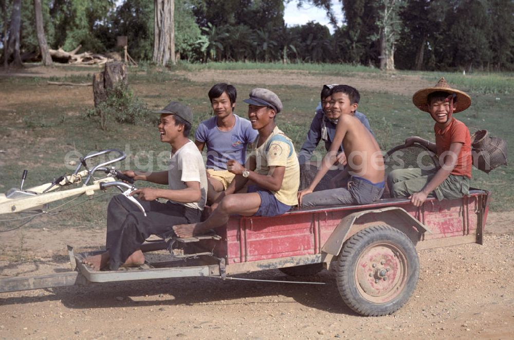Nam Ngum: Auf dem Weg zur Feldarbeit amüsieren sich junge Männer auf dem Anhänger eines elektrischen Karrens in der Demokratischen Volksrepublik Laos.