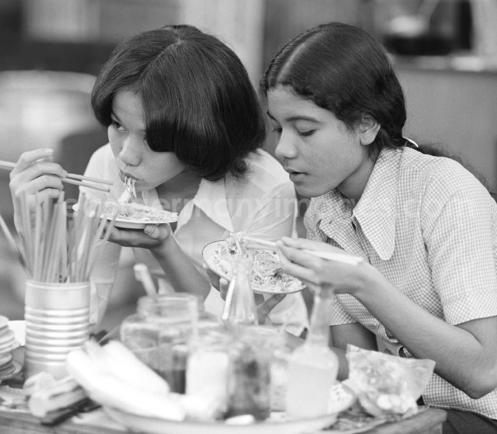 GDR picture archive: Vientiane - Mädchen beim Essen mit Stäbchen auf einem Markt in Vientiane, der Hauptstadt der Demokratischen Volksrepublik Laos.