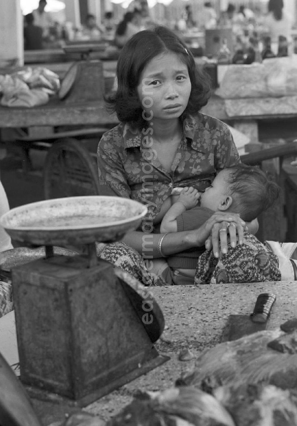 GDR picture archive: Vientiane - Marktszene in Vientiane, der Hauptstadt der Demokratischen Volksrepublik Laos - eine Frau am Verkaufsstand beim Stillen ihres Babys.