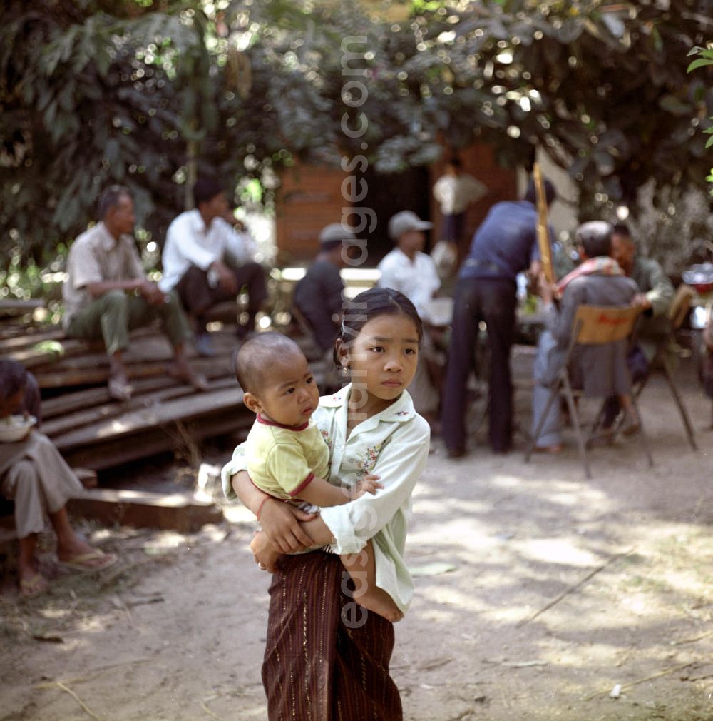 GDR picture archive: Vientiane - Ein Mädchen mit Baby auf dem Arm während einer Hochzeit in einem Dorf in der Demokratischen Volksrepublik Laos.