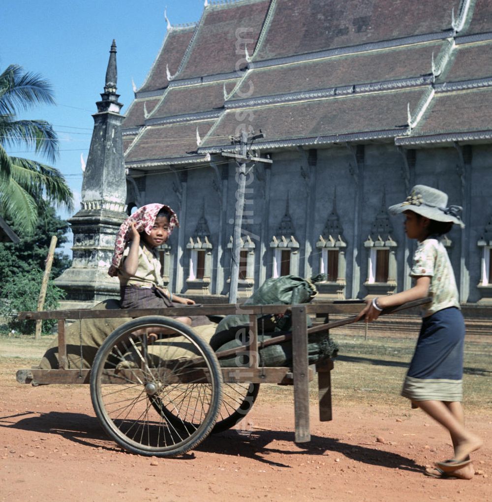 GDR photo archive: Vientiane - Kinder mit Karren vor einem zur goldenen Stupa Pha That Luang gehörenden Tempel in Vientiane, der Hauptstadt der Demokratischen Volksrepublik Laos.