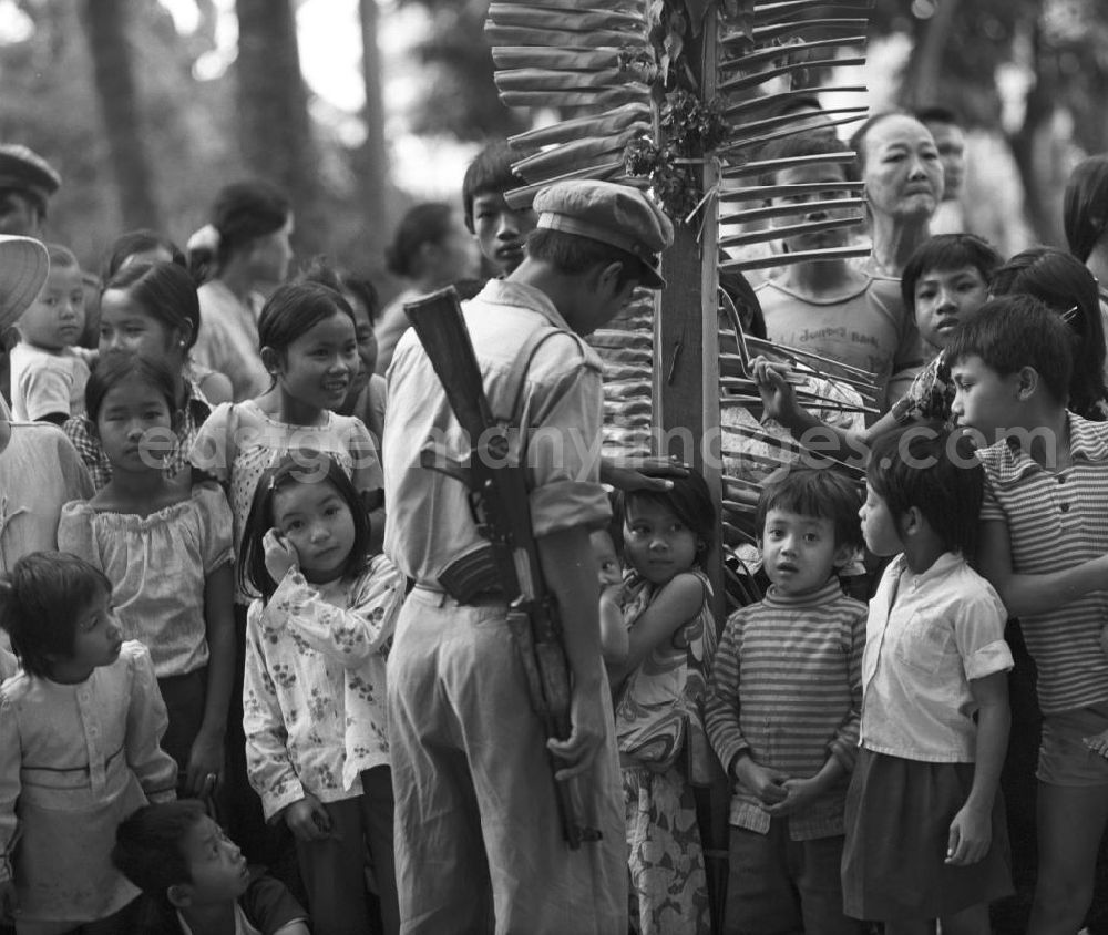 GDR photo archive: Vientiane - Ein Milizionär streichelt einem Mädchen über den Kopf, das zusammen mit anderen Kindern und Familien in Vientiane auf die Rückkehr der umerzogenen Männer und Frauen von der Frauen- und Männerinsel in der Demokratischen Volksrepublik Laos wartet. Das Nam Ngum Reservoir entstand mit der Fertigstellung des gleichnamigen Staudamms im Jahr 1971. Die im See liegenden Inseln dienten in den 7