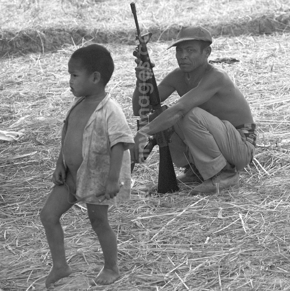GDR picture archive: Vientiane - Ein Angehöriger der laotischen Armee bewacht die Reisernte auf einem Feld in der Demokratischen Volksrepublik Laos. Erst zwei Jahre zuvor, am 2. Dezember 1975, war durch die kommunistisch geprägten Kräfte die Volksrepublik Laos ausgerufen worden. Die politische und wirtschaftliche Situation blieb aber auch in den Folgejahren unsicher und instabil.