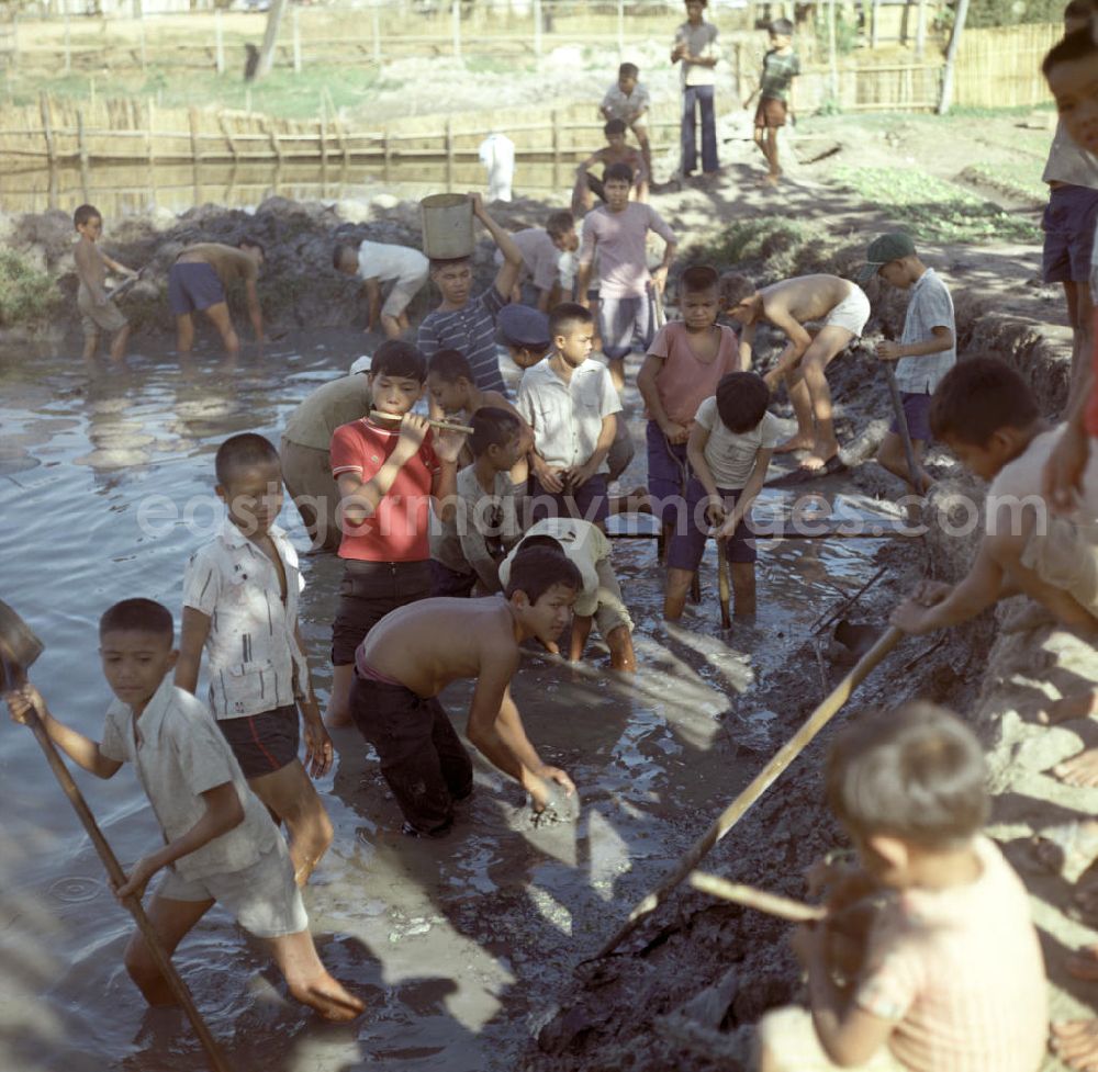 GDR photo archive: Vientiane - Schulkinder graben einen Fischteich und werden dabei von Flötenspielern begleitet in der Demokratischen Volksrepublik Laos.