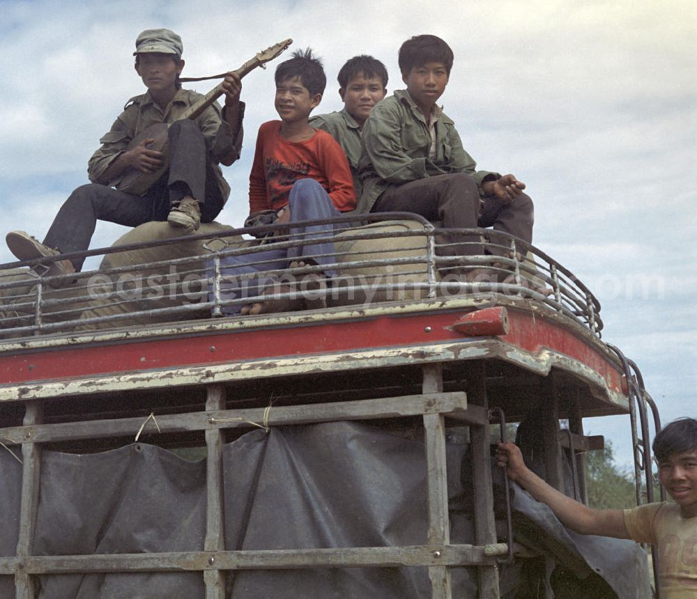 Vientiane: Junge Männer und ein Lautenspieler sitzen auf dem Dach eines Transporters in der Demokratischen Volksrepublik Laos.