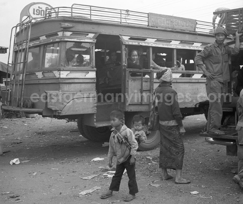 GDR image archive: Vientiane - Ein Junge trägt seinen kleinen Bruder in einem Tragetuch auf dem Rücken vor einem Bus auf einem Markt in Vientiane in der Demokratischen Volksrepublik Laos.