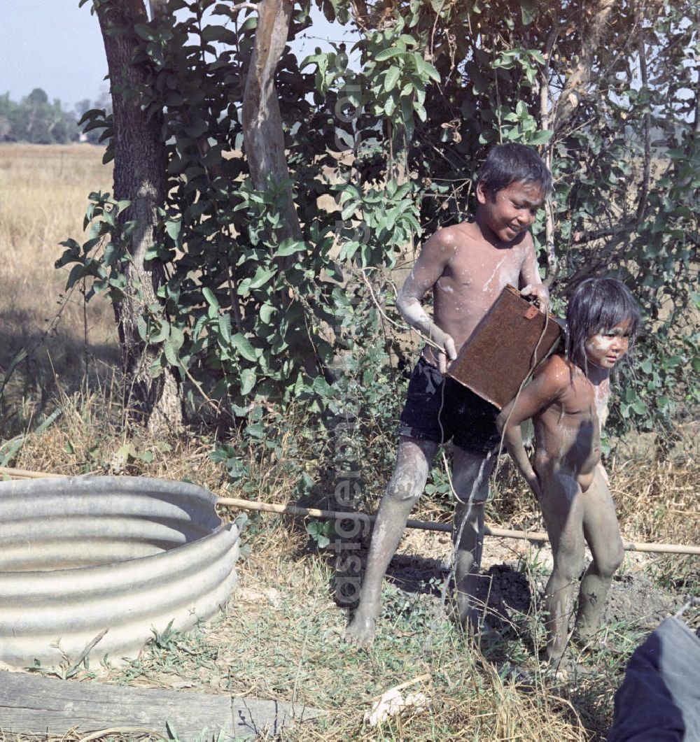 GDR picture archive: Vientiane - Mit Wasser aus einem Brunnen waschen sich zwei Kinder Dreck von ihren Körpern.