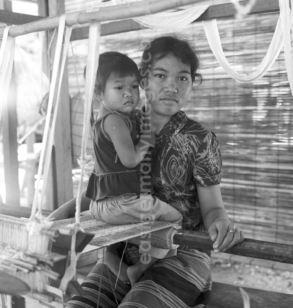 GDR picture archive: Vientiane - Eine Frau mit ihrem kleinen Kind an einem Holzwebstuhl in einer Weberei in Vientiane, der Hauptstadt der Demokratischen Volksrepublik Laos.