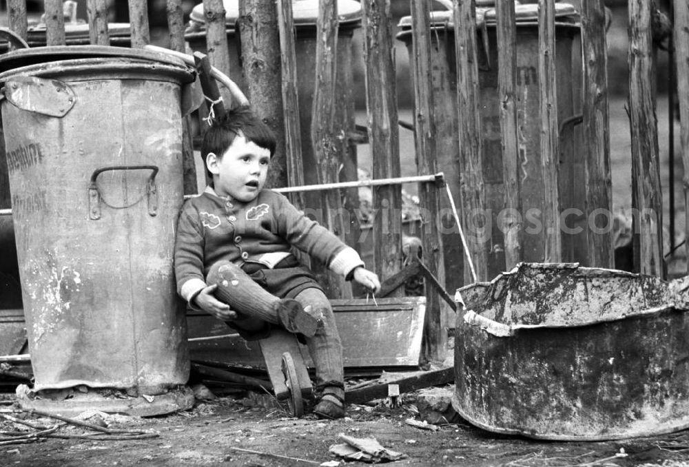 GDR photo archive: Leipzig - Ein Kind sitzt auf seinem Holzroller in einer dreckigen Ecke neben einer alten Mülltonne. Den Jungen scheint der Müll nicht zu stören - er genießt die kleine Pause vom Rollerfahren.