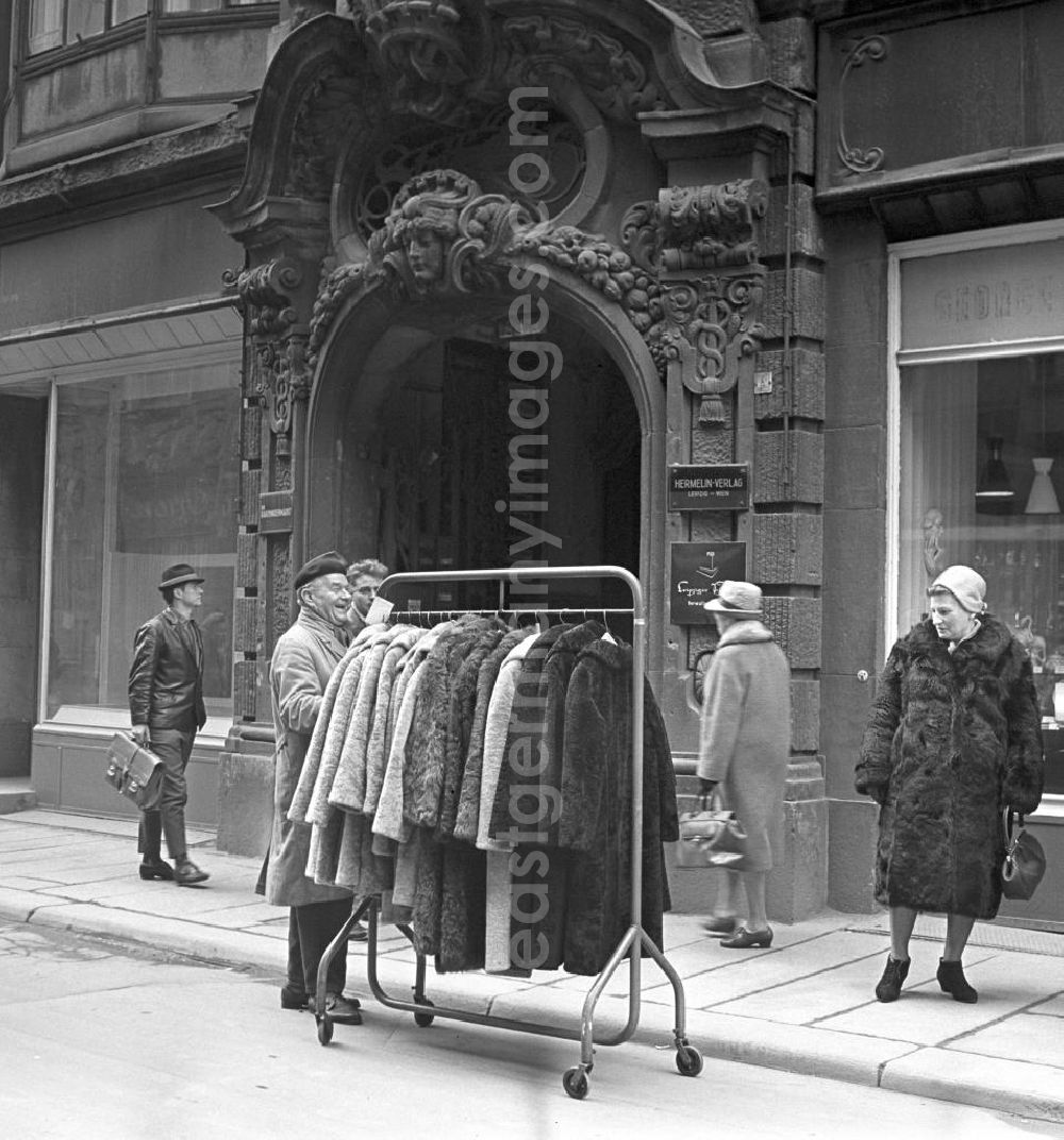 Leipzig: Eine Frau im Pelzmantel betrachtet interessiert neue schicke Pelzmäntel, die auf einem mobilen Kleiderständer durch die Leipziger Innenstadt gefahren werden.