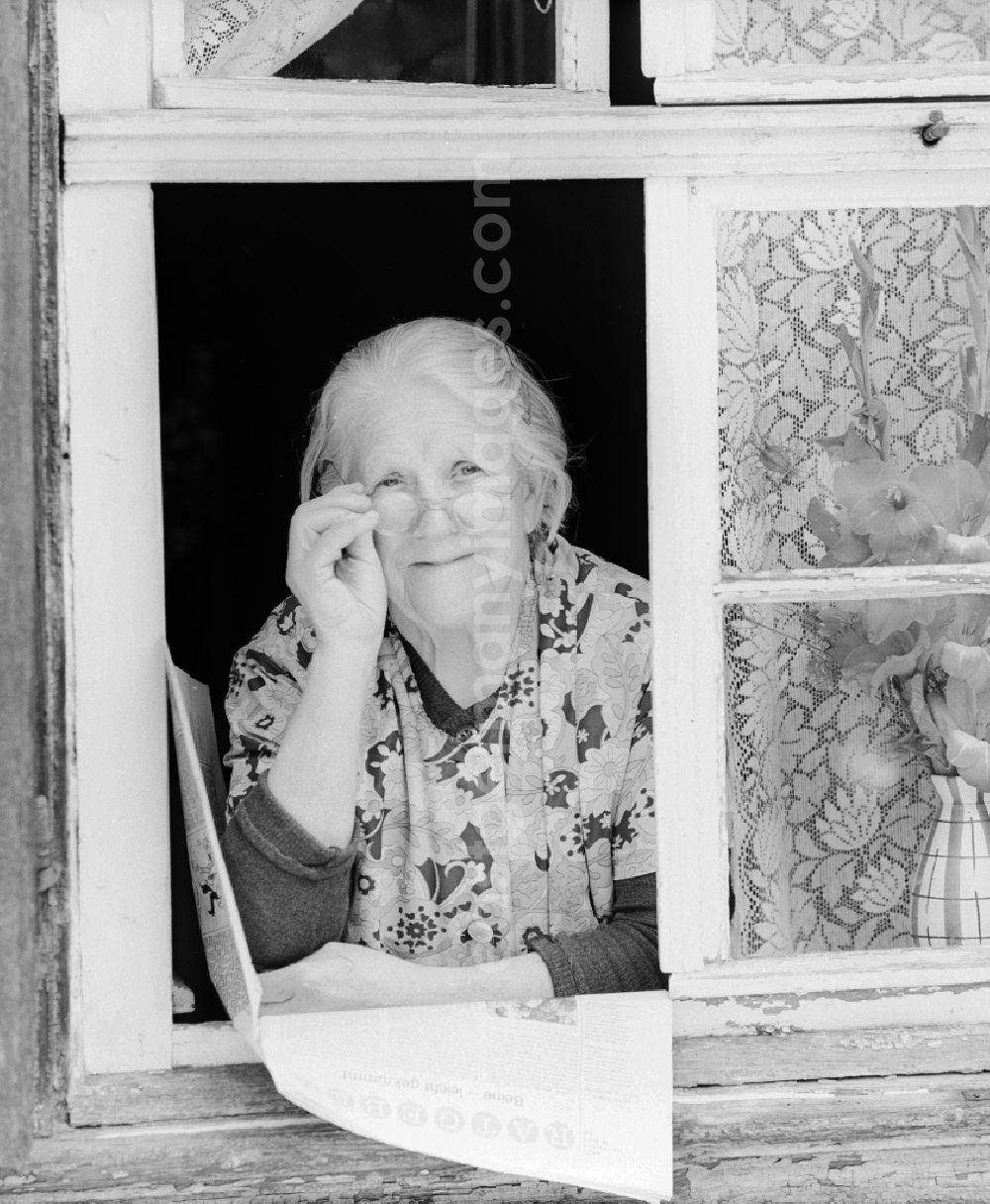 GDR image archive: Quedlinburg - Mature woman with coat apron and glasses looks out of a window in Quedlinburg in the state of Saxony-Anhalt on the territory of the former GDR, German Democratic Republic