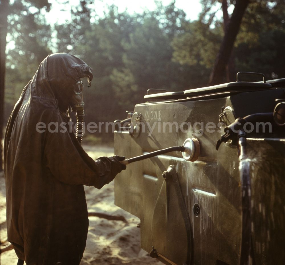 GDR photo archive: Peenemünde - Maneuver exercise of NVA troops of the chemical defense (NBC) in Peenemuende in Mecklenburg-Western Pomerania. A soldier in protective suit (NBC suit, rubber suit) with gas mask in the deactivation (decontamination, decontamination) a contaminated vehicle. Best quality according to original artwork!