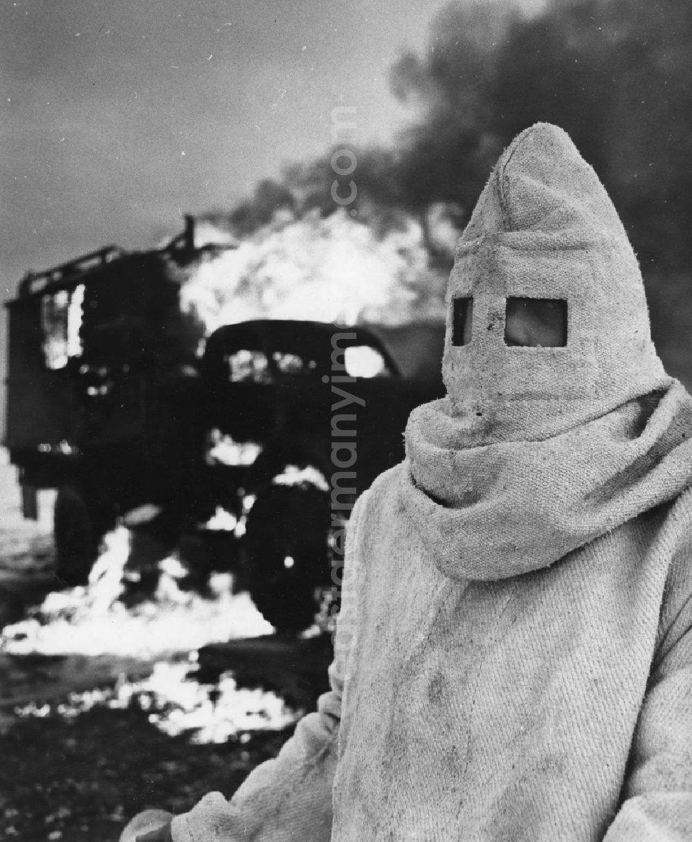 Peenemünde: Maneuver exercise of NVA troops of the chemical defense (NBC) in Peenemuende in Mecklenburg-Vorpommern. In the foreground a soldier in a asbestos and fire resistant protective clothing. In the background burning objects