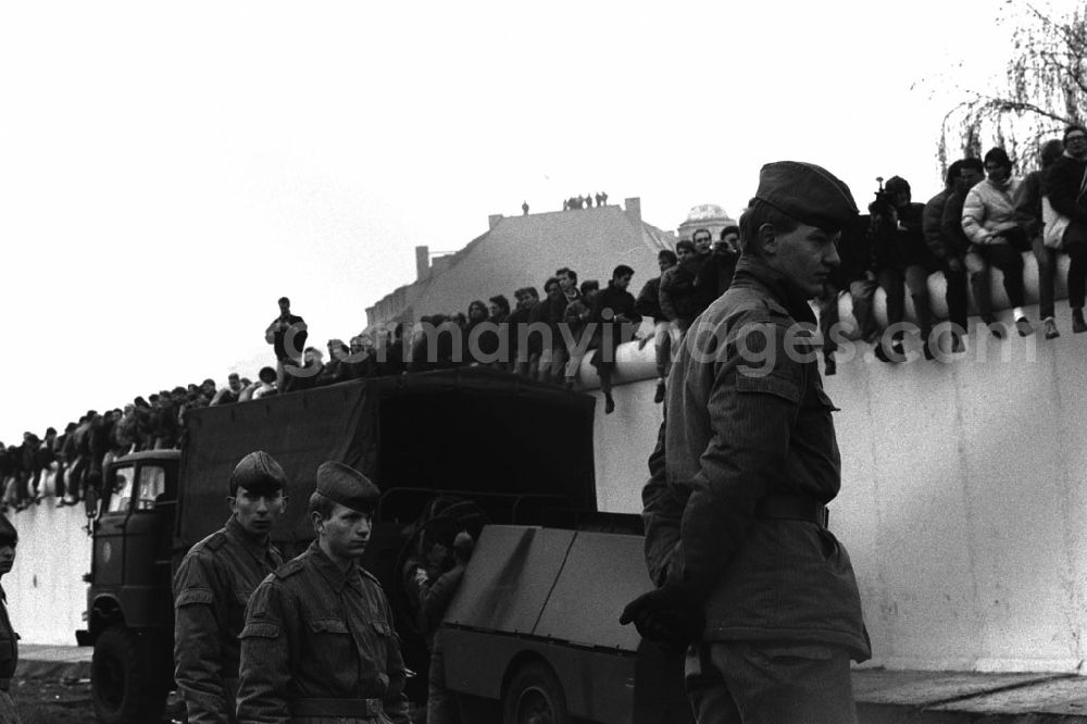 Berlin: Besetzung der Grenzanlagen am Potsdamer Platz. Soldaten der DDR stehen vor der Berliner-Mauer, auf der Mauer sitzen und stehen Menschen.