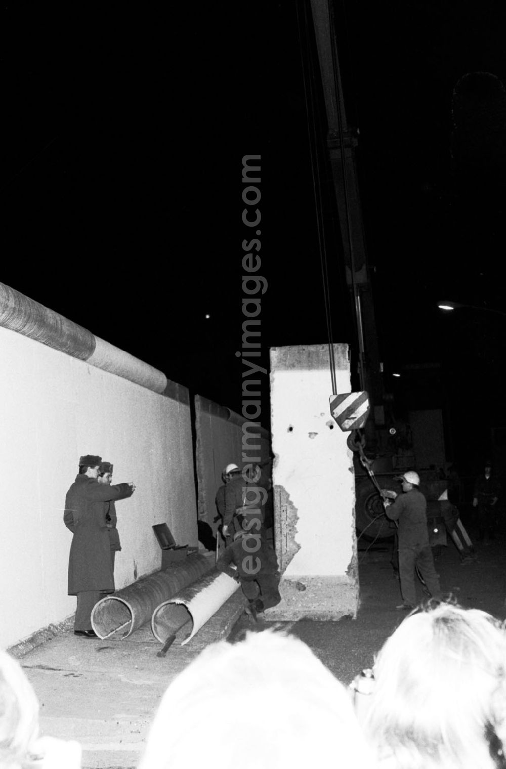 GDR image archive: Berlin - Nachtaufnahme: DDR-Grenzer schlagen eine Lücke in die Mauer am Brandenburger Tor. Ein Mauerstück / Mauer-Element wird an Hacken vom Kran befestigt. In Gegenwart des Bundeskanzlers und des Ministerpräsidenten der DDR wird an dieser symbolträchtigen Stelle ein Grenzübergang für Fußgänger eröffnet. Menschenmengen auf beiden Seiten bejubeln jedes herausgehobene Betonelement. Fotos und TV-Aufnahmen dieses Ereignisses werden später oft fälschlich als Abriss der Mauer beschrieben, obwohl es sich nur um die Einrichtung neuer Grenzübergänge handelte. Erst im Juni beginnt der offizielle Abriss.