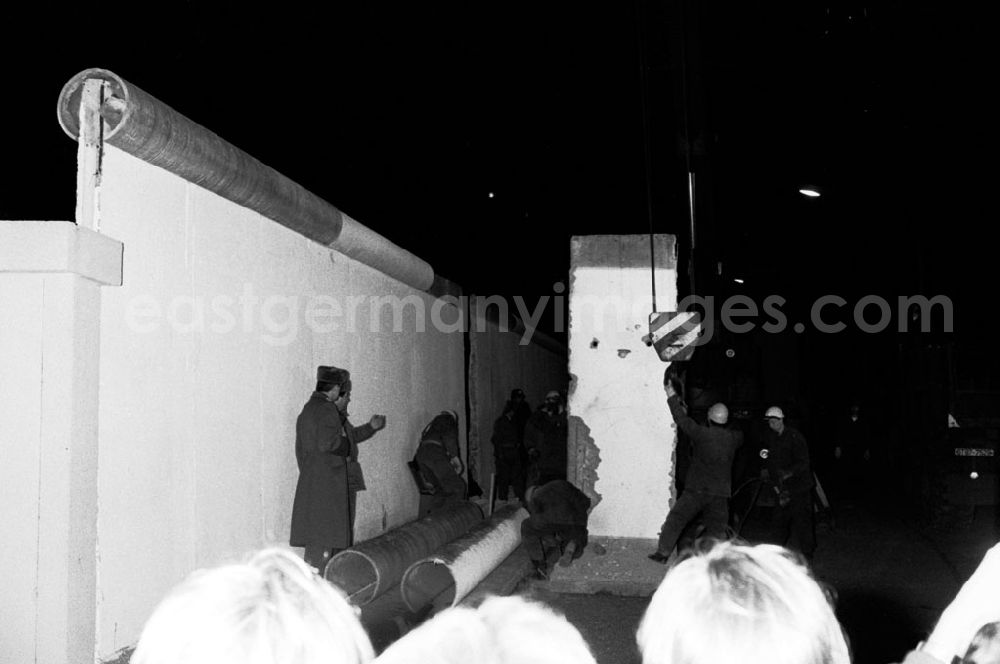 GDR photo archive: Berlin - Nachtaufnahme: DDR-Grenzer schlagen eine Lücke in die Mauer am Brandenburger Tor. Ein Mauerstück / Mauer-Element wird an Hacken vom Kran befestigt. In Gegenwart des Bundeskanzlers und des Ministerpräsidenten der DDR wird an dieser symbolträchtigen Stelle ein Grenzübergang für Fußgänger eröffnet. Menschenmengen auf beiden Seiten bejubeln jedes herausgehobene Betonelement. Fotos und TV-Aufnahmen dieses Ereignisses werden später oft fälschlich als Abriss der Mauer beschrieben, obwohl es sich nur um die Einrichtung neuer Grenzübergänge handelte. Erst im Juni beginnt der offizielle Abriss.