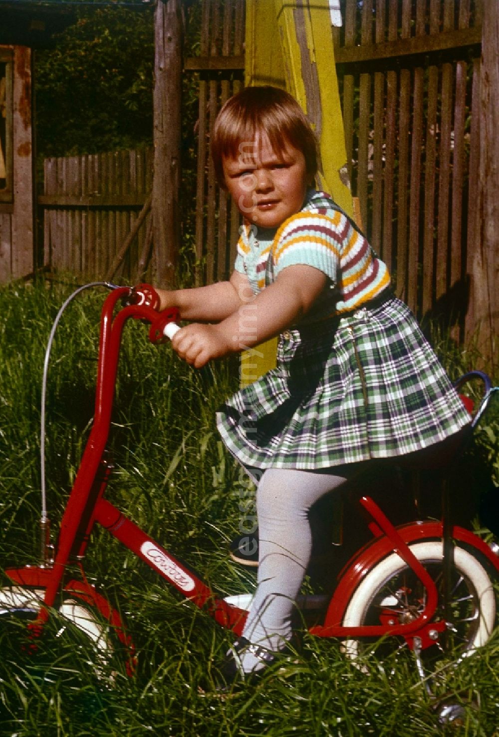 GDR photo archive: Neustrelitz - A girl in the checked rock on a red children's bicycle of the brand Cowboy in Neustrelitz in the federal state Mecklenburg-West Pomerania in the area of the former GDR, German democratic republic