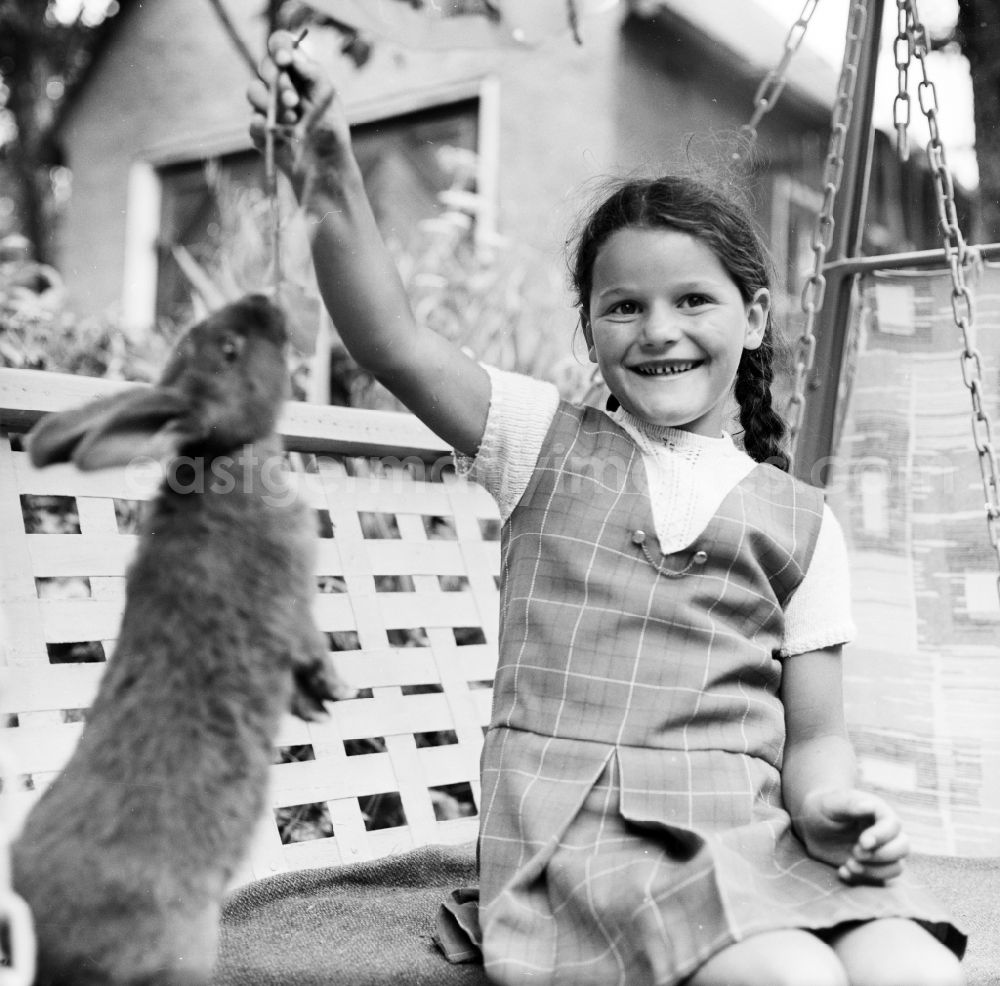 GDR image archive: Scheibenberg - Girl sits with a rabbit of a garden swing in Scheibenberg in the federal state Saxony in the area of the former GDR, German democratic republic