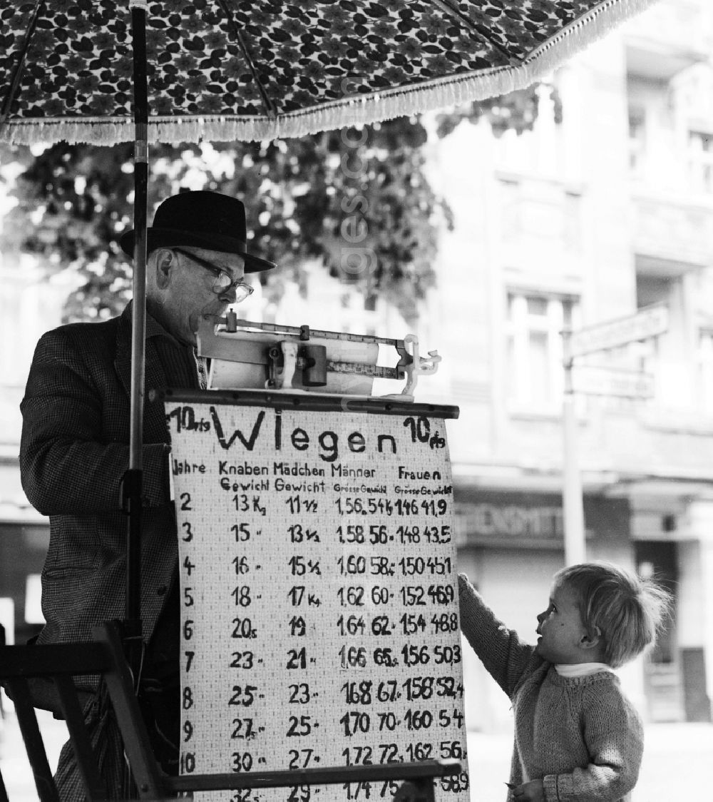 GDR image archive: Berlin - With hat and suit dressed elderly gentleman in weighing of road passersby on the Schoenhauser Allee in Berlin, the former capital of the GDR, German Democratic Republic. A small child looks reverently on the weighing table in front of the scale. For a mite of 1