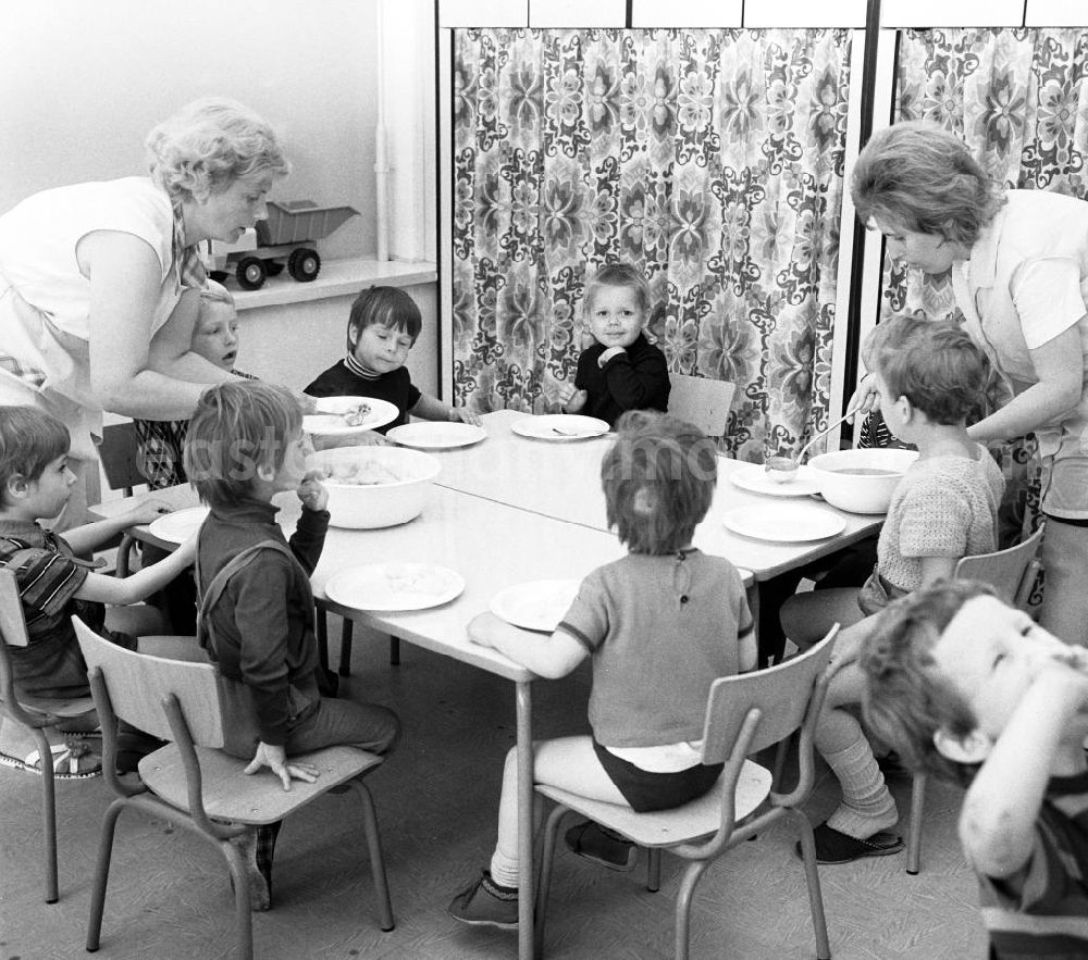 GDR photo archive: Berlin - Kinder bei der Speisung / Essen in einer Kinderkrippe im Neubaugebiet Amtsfeld in Berlin-Köpenick. Die Kinder bekommen von den beiden Erzieherinnen das Essen aufgetan.