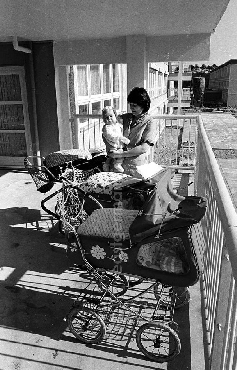 GDR image archive: Berlin - Eine Erzieherin steht auf dem Balkon in einer Kinderkrippe in der Salvador-Allende-Straße in Berlin-Köpenick und hält ein Baby auf dem Arm. Drumherum Kinderwagen mit schlafenden Babys.