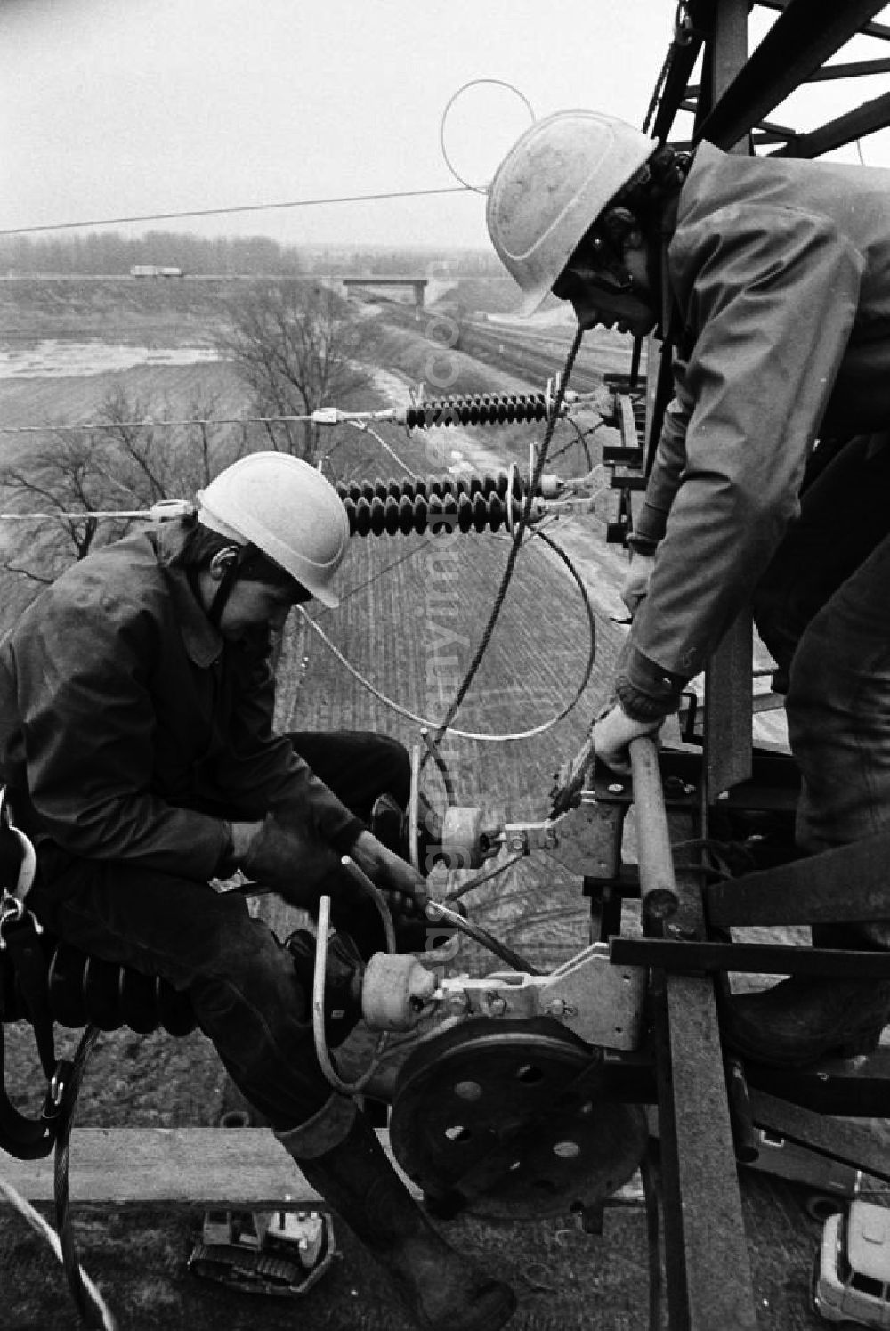 GDR photo archive: Brieselang - Arbeiter bei der Montage einer Hochspannungsleitung bei Brieselang in luftiger Höhe in Aktion. Die DDR-Energieversorung basiert zu einem großen Teil auf der Verstromung von Braunkohle aus der Lausitz und Sachsen, was unter anderem lange Leitungswege nötig macht.