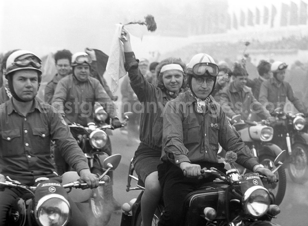 Berlin: Zu Pfingsten 1964, vom 16.-18. Mai, findet in Berlin das letzte Deutschlandtreffen der Jugend für Frieden und Völkerfreundschaft statt. Im Bild festgehalten ein Motorrad-Korso mit diversen Trabant-Motorrädern sowie einer IWL Troll. Eine junge Frau / Jugendliche grüßt mit einer roten Nelke. Die Fahrer sind mit Motorrad-Helmen dieser Zeit ausgestattet. Ziel der ersten Veranstaltung im Mai 1950 war, die kommunistische Jugend in Ost und West mobil zu machen und der damals in der BRD noch zugelassenen FDJ neue Anhänger zuzuführen. 1951 wurde das Verbot gegen die FDJ in der BRD ausgesprochen. Nach 1964 entsprach eine gesamtdeutsche kommunistische Politik nicht mehr den Zielen der DDR-Regierung. In den 70er und 8