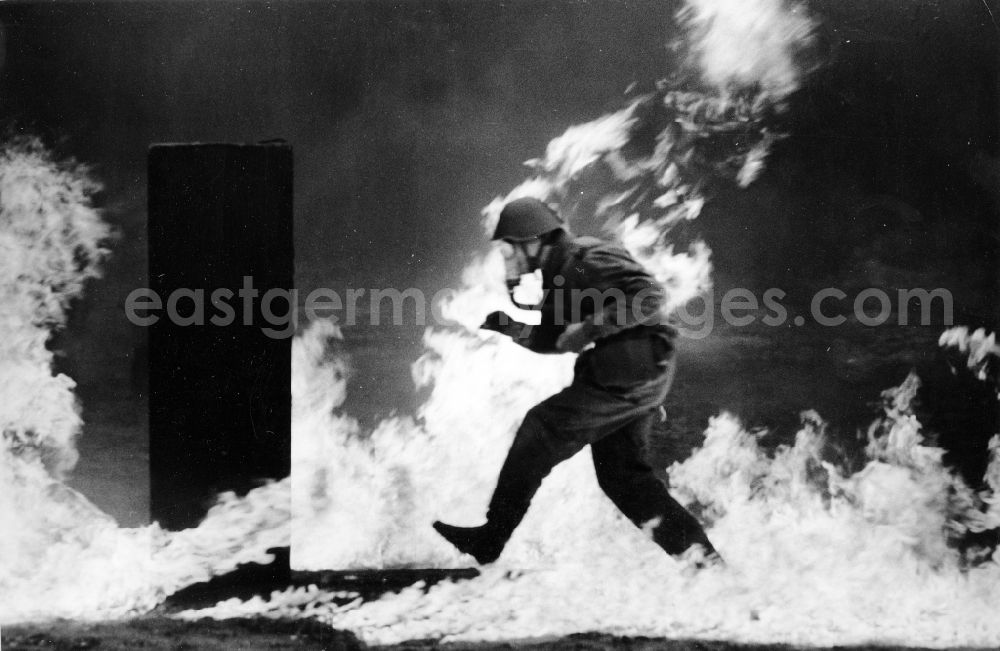 GDR photo archive: Peenemünde - Soldier runs during a maneuver exercise of NVA troops of chemical defense, by a napalm arena with burning objects in Peenemuende in Mecklenburg-Western Pomerania