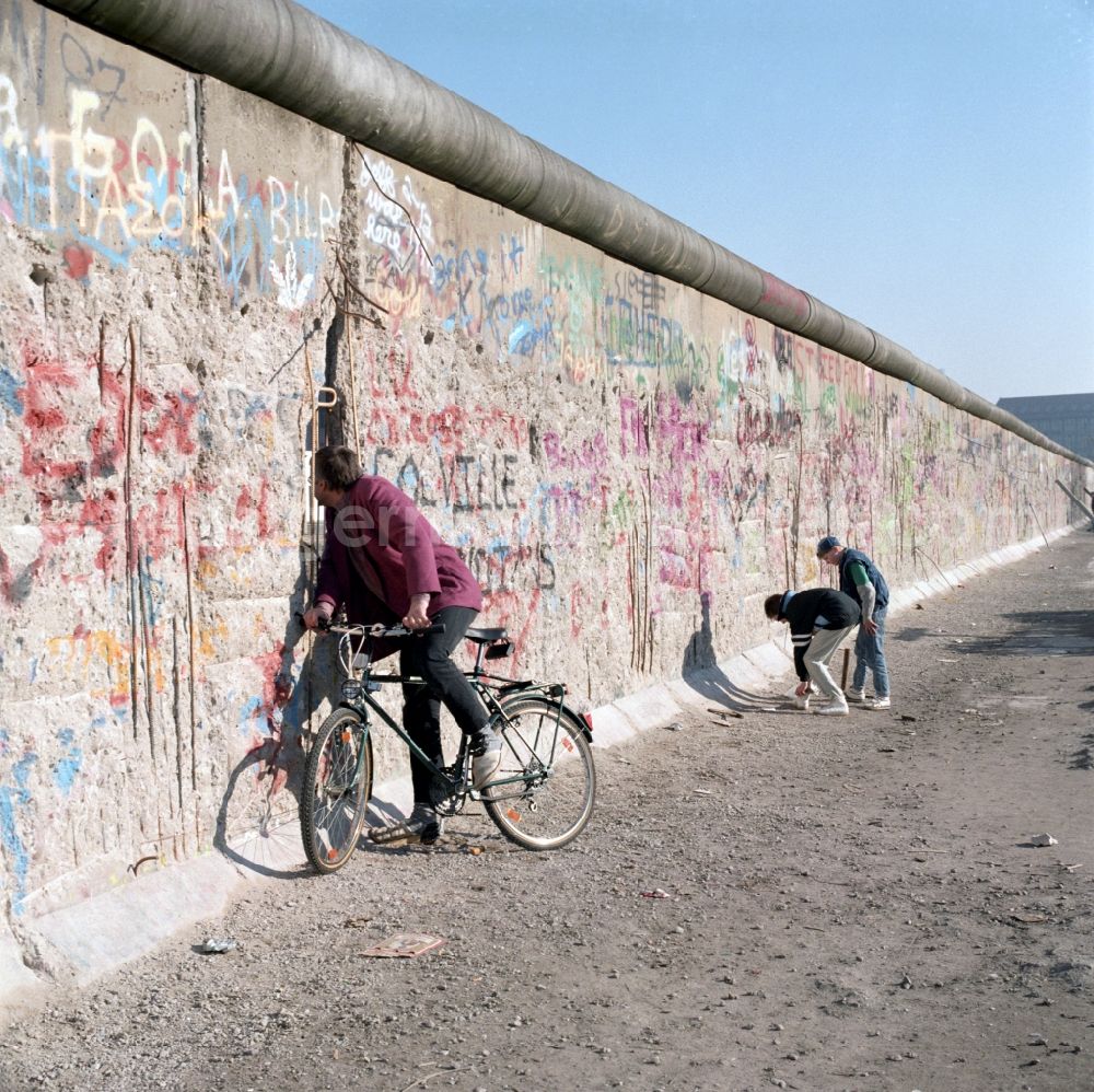 GDR photo archive: Berlin - Curious looks a cyclist through a hole in the Berlin Wall in Berlin