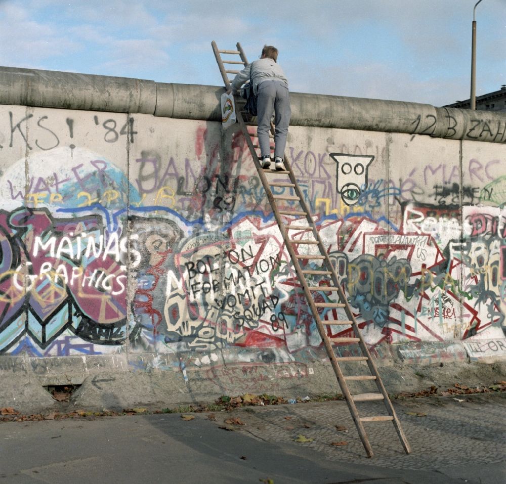 GDR photo archive: Berlin - Mitte - Neugieriger Mann klettert mit Hilfe einer Leiter an der Berliner Mauer hoch. Die Berliner Mauer war während der Teilung Deutschlands ein hermetisch abriegelndes Grenzbefestigungssystem der Deutschen Demokratischen Republik.
