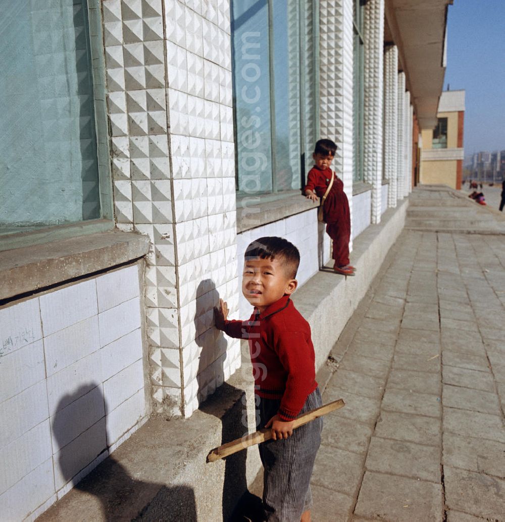 GDR picture archive: Pjöngjang - Kinder an einer Hausfassade auf einer Straße in Pjöngjang, der Hauptstadt der Koreanischen Demokratischen Volksrepublik (KDVR). Im Hintergrund Plattenbauten im sozialistischen Stil. Die nordkoreanische Hauptstadt war nach der Zerstörung im Koreakrieg vor allem mit Unterstützung der Sowjetunion in den 50er und 6