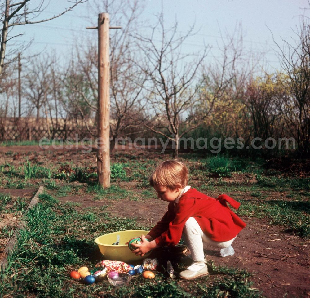 Zschopau: A small child in a red dress with the Easter egg look in the garden in Zschopau in the federal state Saxony in the area of the former GDR, German democratic republic