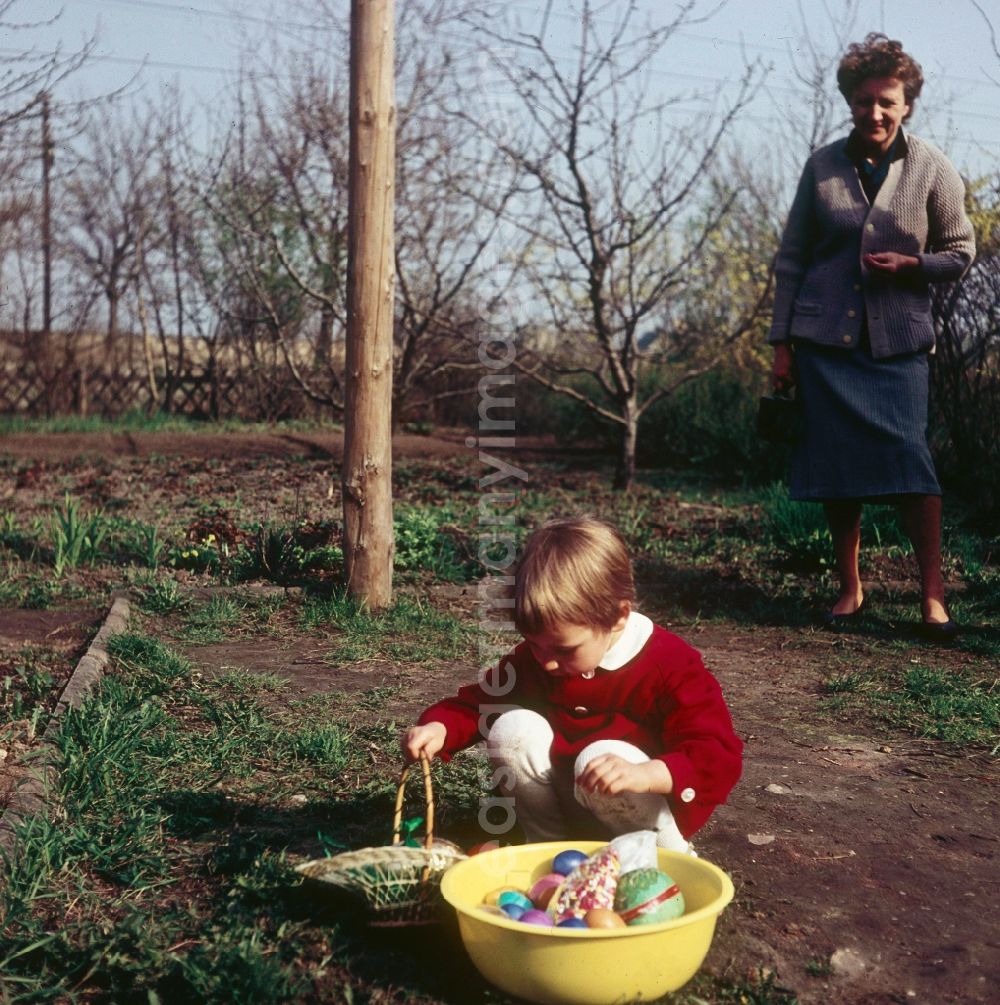 Zschopau: A small child in a red dress with the Easter egg look in the garden in Zschopau in the federal state Saxony in the area of the former GDR, German democratic republic