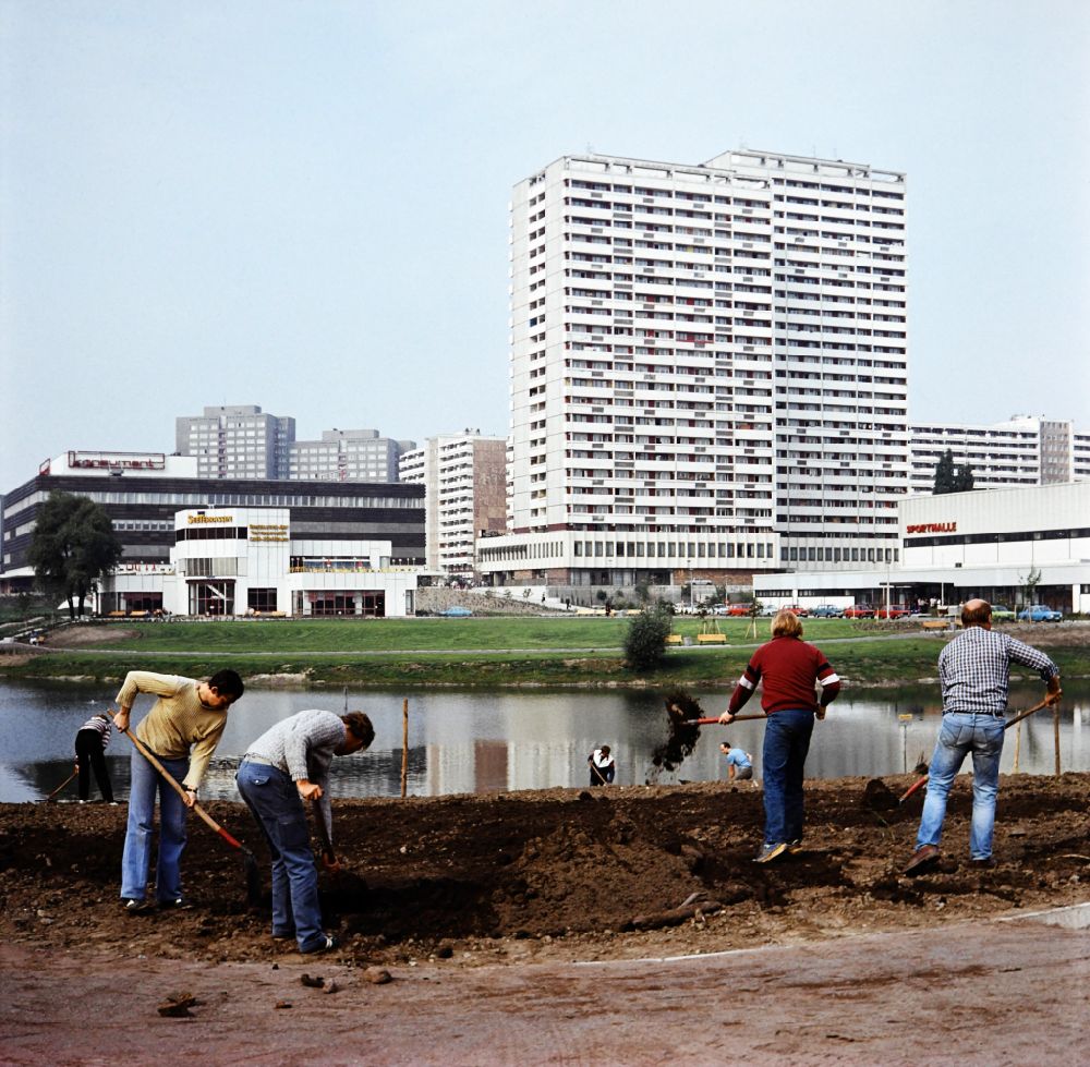 Berlin: Fennpful park in the Lichtenberg district of Eastberlin in the territory of the former GDR, German Democratic Republic. Workers create a new flower bed at the lake. In the background are the lakeside terraces, the consumer department store, apartment buildings and a sports hall