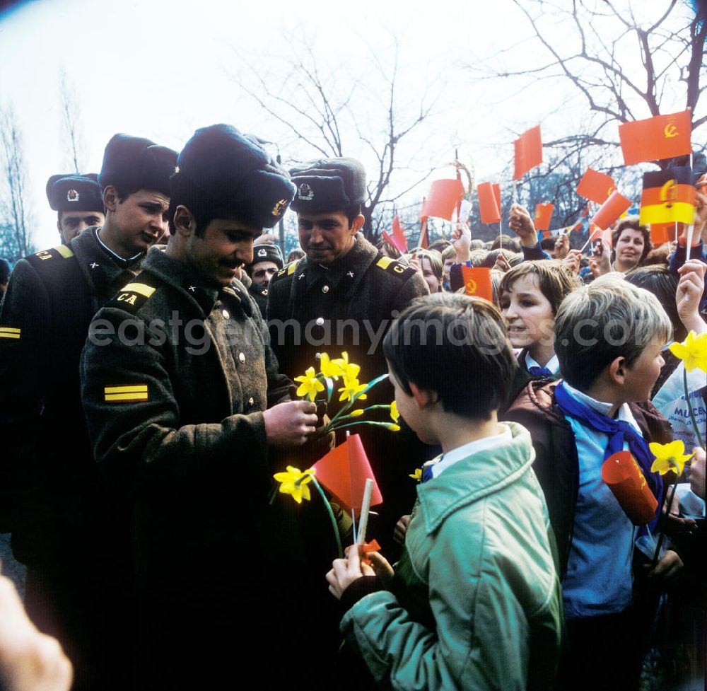 GDR picture archive: Berlin - Pioniere / Jungpioniere übergeben Blumen an sowjetische Soldaten anlässlich zum Tag der Befreiung. Schaulustige mit Winkelementen im Hintergrund, Flagge Sowjetunion und DDR.