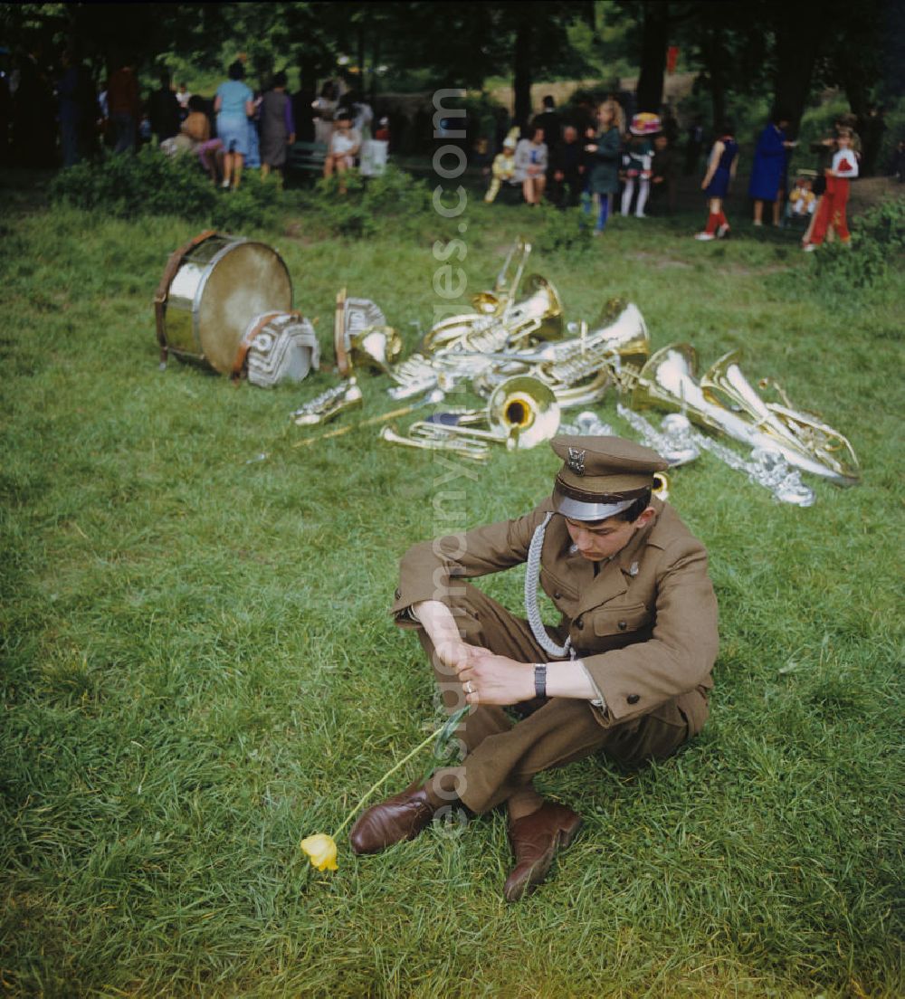 GDR picture archive: Gubin - Zum Festprogramm des Frühlingsfestes in Gubin sitzt ein Mitglied der Musikkappelle mit einer Tulpe in der Hand vor den im Gras liegenden Blechblasinstrumenten.