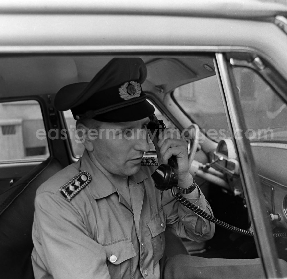 GDR photo archive: Berlin - Policeman in uniform of the VP People's Police - Master Reinhold Guenther with a telephone receiver in a radio conversation in a radio patrol car GAZ M21 Volga in the district of Pankow in Berlin East Berlin on the territory of the former GDR, German Democratic Republic