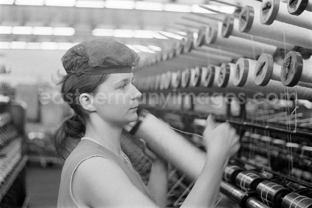 GDR picture archive: Fürstenwalde/Spree - Female worker with hairnet changes a coil on a direct cabling machine for tire cord in the production plant and operating facilities of the VEB Reifenkombinat Fuerstenwalde, later Pneumant Reifen Gmbh and Goodyear, in Fuerstenwalde/Spree in the state Brandenburg on the territory of the former GDR, German Democratic Republic