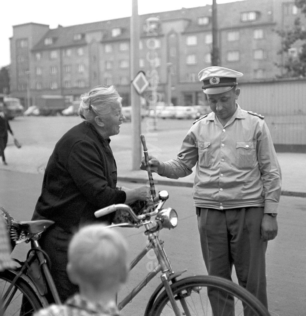 GDR picture archive: Rostock - Eine alte Frau ist mit ihrem Fahrrad auf einer Straße in Rostock gestürz, ein Verkehrspolizist hilft ihr wieder auf die Beine. Der Einkaufsbeutel am Lenkrad hatte sich in den Speichen verfangen.
