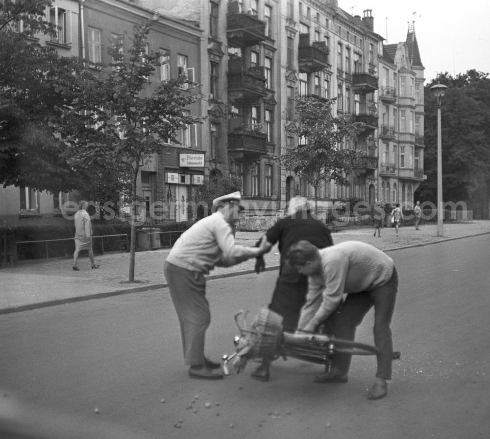 GDR image archive: Rostock - Eine alte Frau ist mit ihrem Fahrrad auf einer Straße in Rostock gestürz, ein Passant und ein Verkehrspolizist helfen ihr wieder auf die Beine. Der Einkaufsbeutel am Lenkrad hatte sich in den Speichen verfangen.