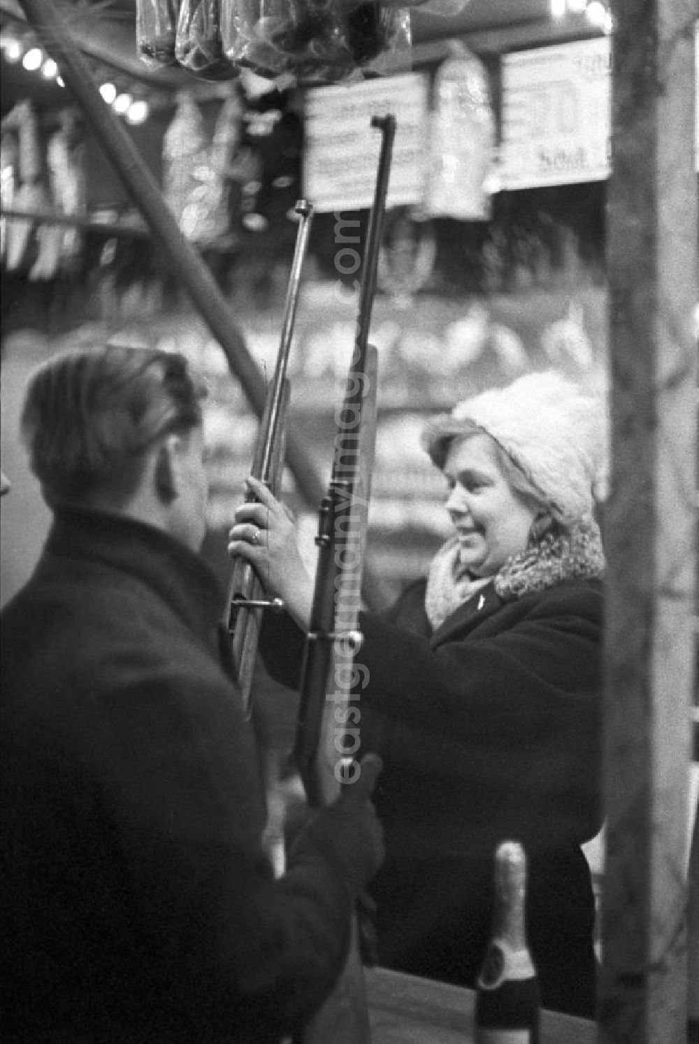 GDR photo archive: Leipzig - Eine Schaustellerin des Schießstandes auf dem Leipziger Weihnachtsmarkt hilft den Kunden beim Laden des Gewehres.
