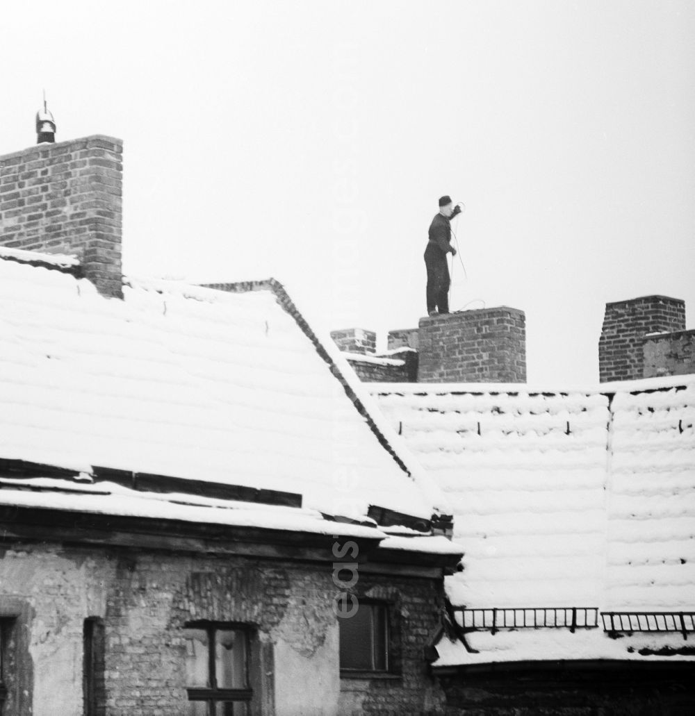 GDR picture archive: Berlin - A chimney sweep on snow-covered roofs round the chimneys in Berlin, the former capital of the GDR, German Democratic Republic