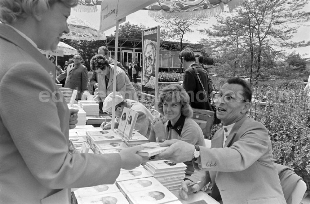 Erfurt: Writers' bazaar on the grounds of the IGA in the Rose Garden on the occasion of the 15th Workers' Festival in Erfurt in the federal state of Thuringia in the territory of the former GDR, German Democratic Republic. Herbert Jobst (author) signs his book Der Gluecksucher at the book bazaar. In the background the writer Bernhard Seeger