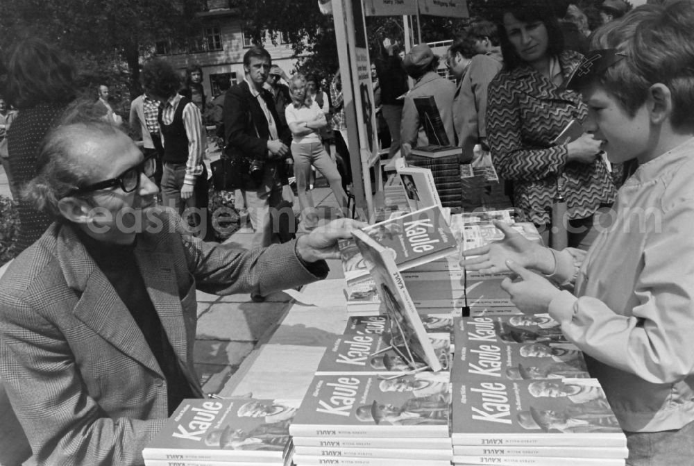 GDR picture archive: Erfurt - Writers' bazaar on the grounds of the IGA in the Rose Garden on the occasion of the 15th Workers' Festival in Erfurt in the federal state of Thuringia in the territory of the former GDR, German Democratic Republic. Alfred Wellm ( known in the GDR mainly as a children's author ) signs his book Kaule for a boy at the book bazaar
