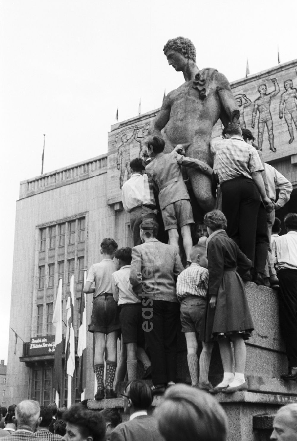 GDR photo archive: Berlin - A group of children and Judendlichen stand on the base of the sculpture and copy of a late-classicistic male figure before the entrance of the gymnasium in the Stalin's avenue in Berlin, the former capital of the GDR, German democratic republic