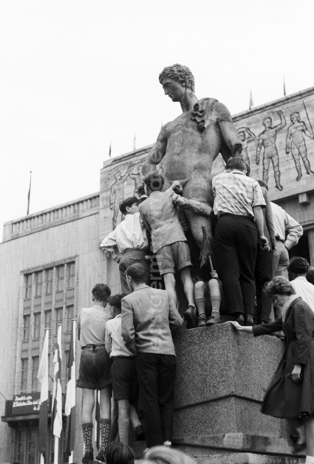 GDR picture archive: Berlin - A group of children and Judendlichen stand on the base of the sculpture and copy of a late-classicistic male figure before the entrance of the gymnasium in the Stalin's avenue in Berlin, the former capital of the GDR, German democratic republic