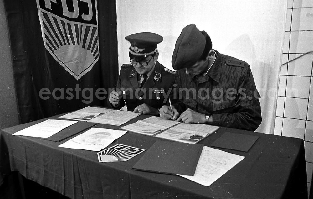 Karlshagen: Soldier and ensign in the uniform of the LSK/LV Air Force of the FTB-9 Aviation Technical Battalion of the NVA in front of an FDJ flag at a table in Karlshagen, Mecklenburg-Western Pomerania in the area of the former GDR, German Democratic Republic