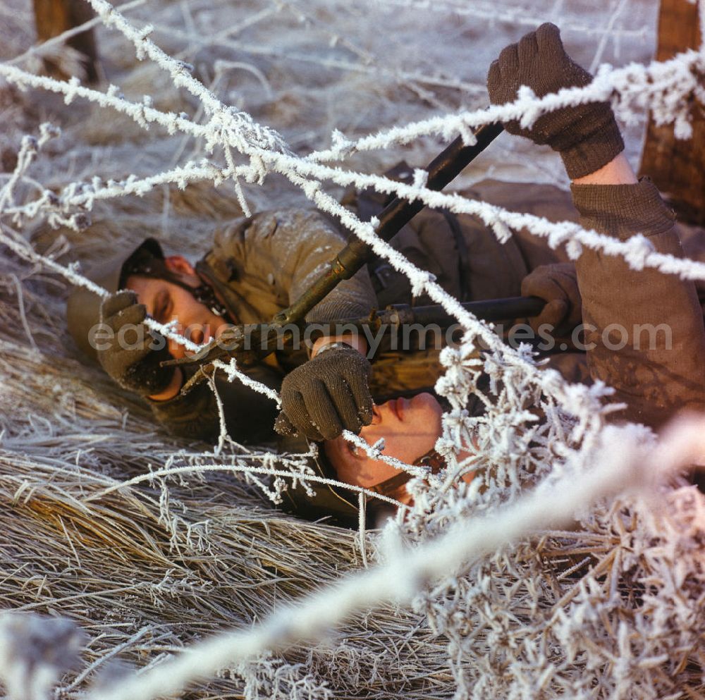 GDR image archive: Storkow - Soldaten der NVA durchdringen einen Stacheldrahtzaun / Zaun bei einer Übung im Winter.