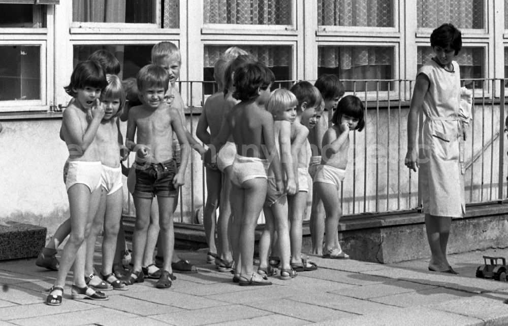 GDR photo archive: Berlin - Summer temperatures while playing and having fun with toddlers cared for by educators in a kindergarten on a playground in Berlin East Berlin on the territory of the former GDR, German Democratic Republic