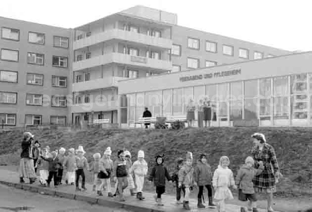 GDR picture archive: Beeskow - Zur Faschingszeit kostümierte Kinder laufen in Begleitung von zwei Erzieherinnen an einem Pflegeheim für Senioren vorbei. Rentnerinnen / Senioren / Omas stehen vor Pflegeheim und schauen den Kindern hinterher.